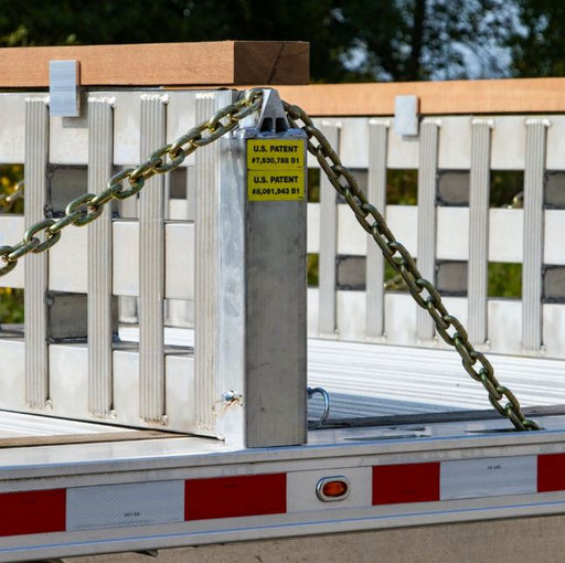 Left-side aluminum load leveler stake measuring 4-1/8 inches long, 4-1/8 inches wide, and 18-1/4 inches high; weighs 10 lbs and fits 3/8-inch chain for securing step deck trailer ramps.